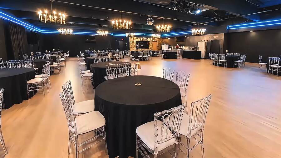 Crown Prince Event Hall in San José — round banquet tables with clear chairs under chandeliers and blue cove lighting